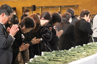 参列者の方々が献花台に献花を行い、手を合わせて祈りを捧げている様子を写した写真