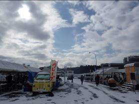 雪の積もった会場の通路脇に黄色いクレープの移動販売車が停まっている写真
