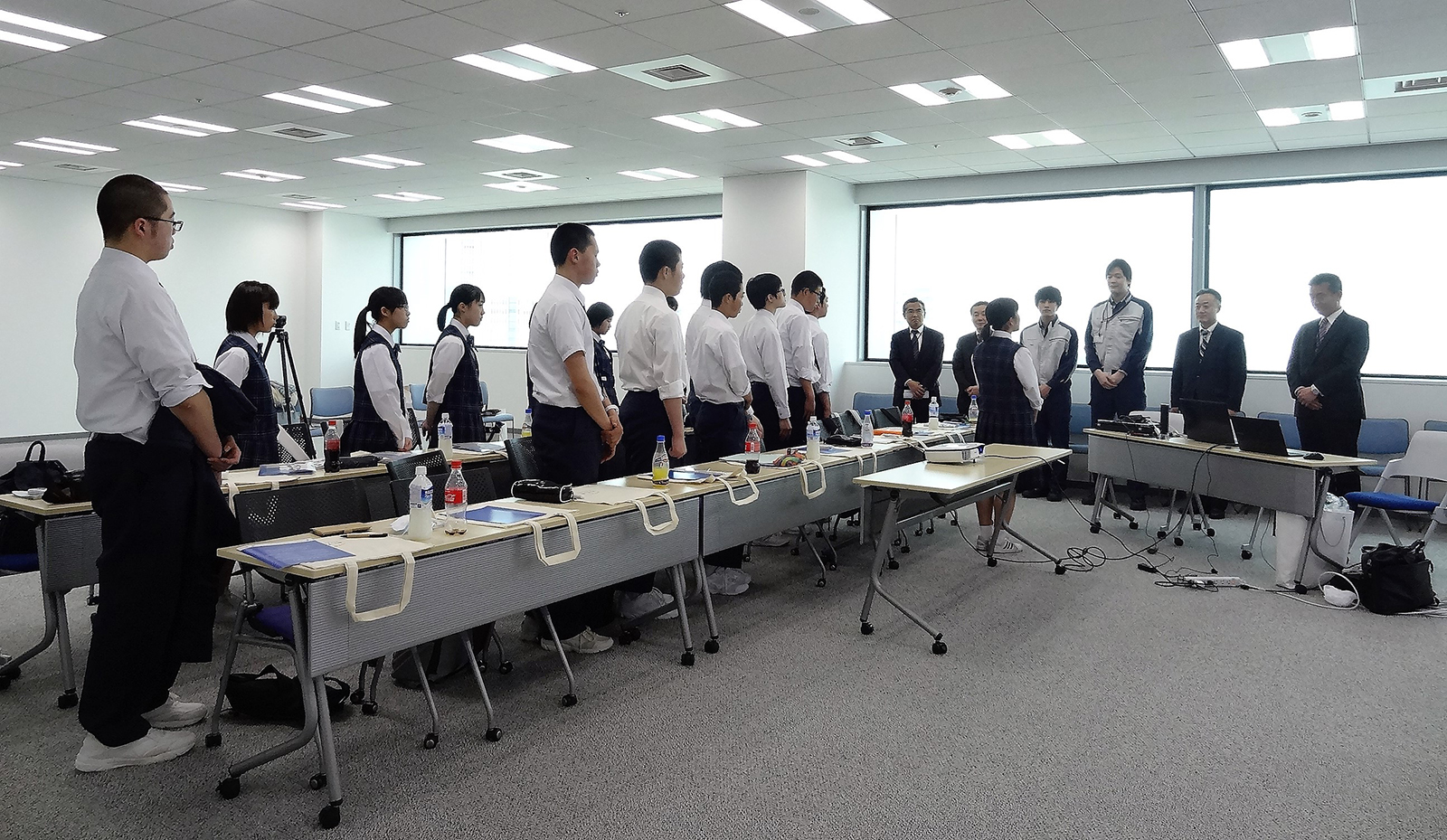 生徒たちと関係者が会議室で向かい合って立っている写真