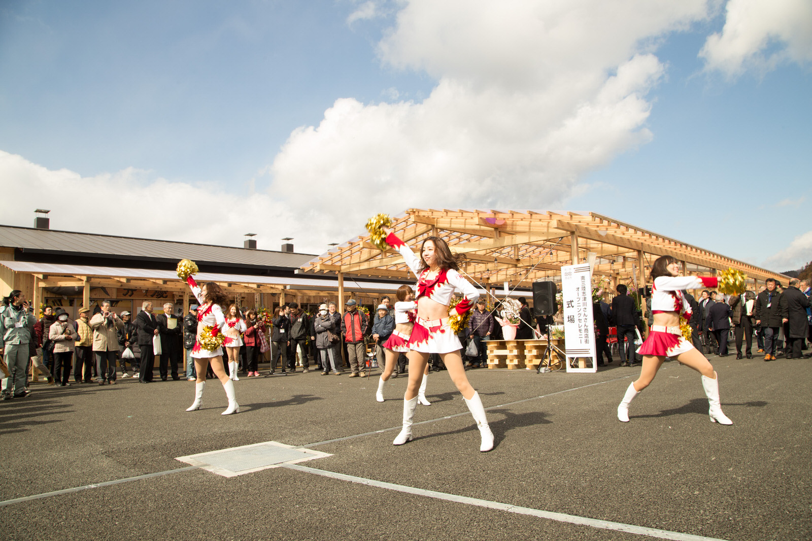 観客が立ち並ぶ屋外で、赤と白の衣装を着たチアリーダーが元気にパフォーマンスをしているオープニングイベントの写真