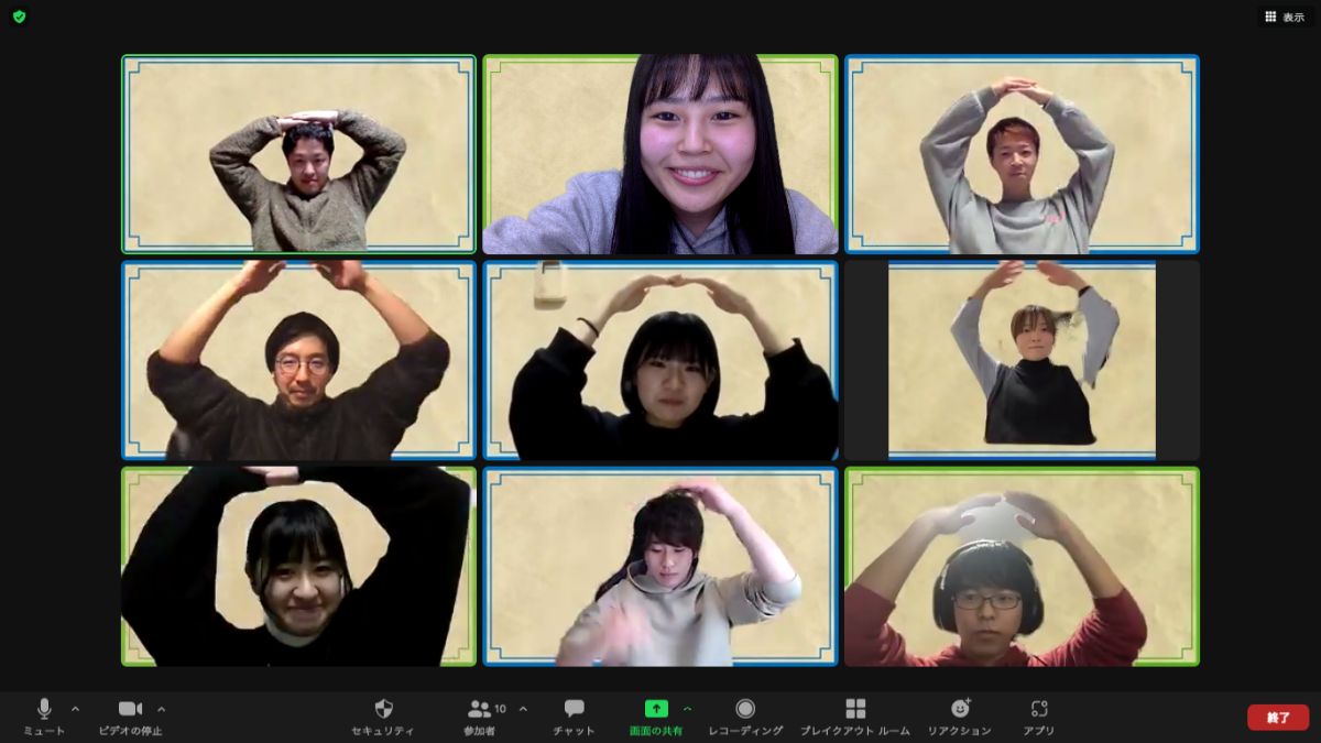 画面に9人の参加者の画面がタイル状に並んで表示され、真ん中上の女性以外の全員が両手を頭の上で丸くして「OK」のポーズを取りながら笑顔を見せているZoom画面の画像