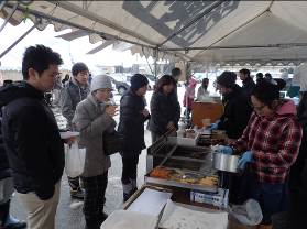 食べ物の屋台のテントに防寒着を着た、寒そうな様子の来場者が並んでいる写真