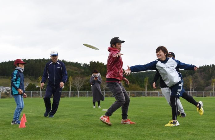 緑の芝生を全面に敷き詰めた広場で5人の方がフリスビーを投げ遊んでいる写真