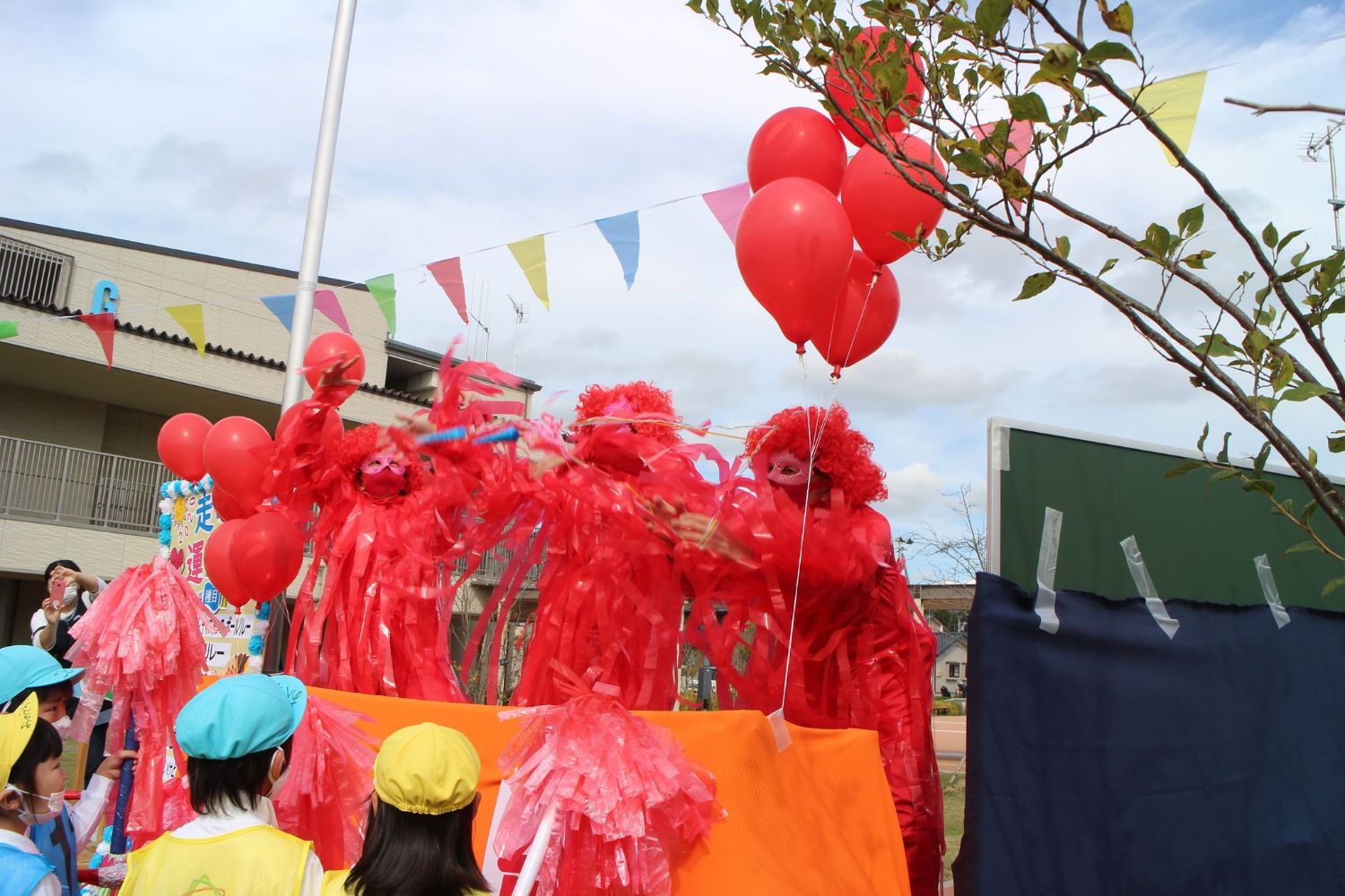 赤いかつらと赤い衣装を着て赤い風船を持ち聖火のパフォーマンスをしている様子の写真