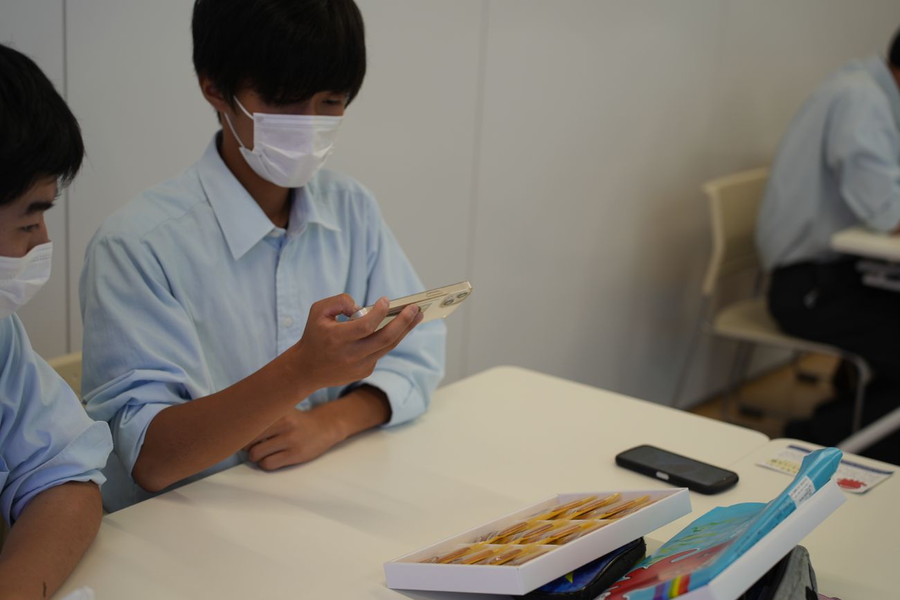 高校生2人が机に向かい合い、スマートフォンを見ながら何かを確認している様子の写真