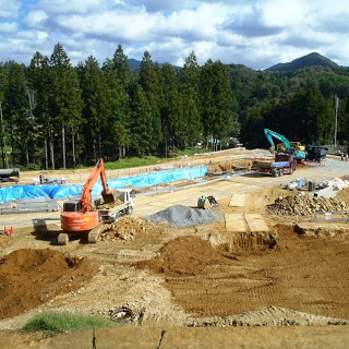 数台の重機が並んで土をならし、青いシートで囲われたエリアも見える住宅地の整備が進んでいる造成工事中の写真