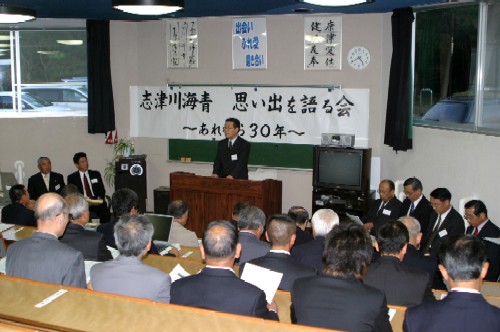 「志津川海青 思い出を語る会 」と書かれた横断幕の下、壇上に立つ男性が多数の参加者を前に話をしている様子の写真