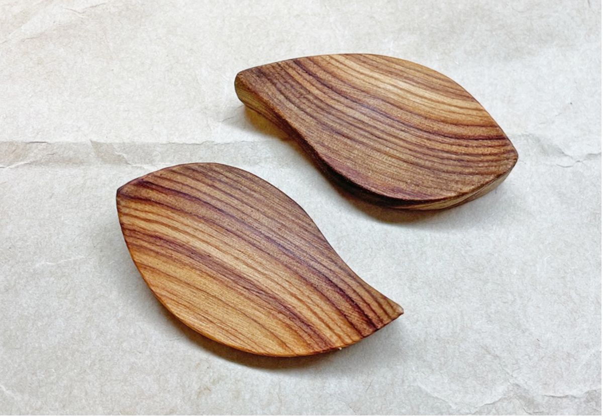 光沢のある仕上がりになった木目の美しい葉型パーツが2つ置かれている、オイル塗布後の木製パーツの写真