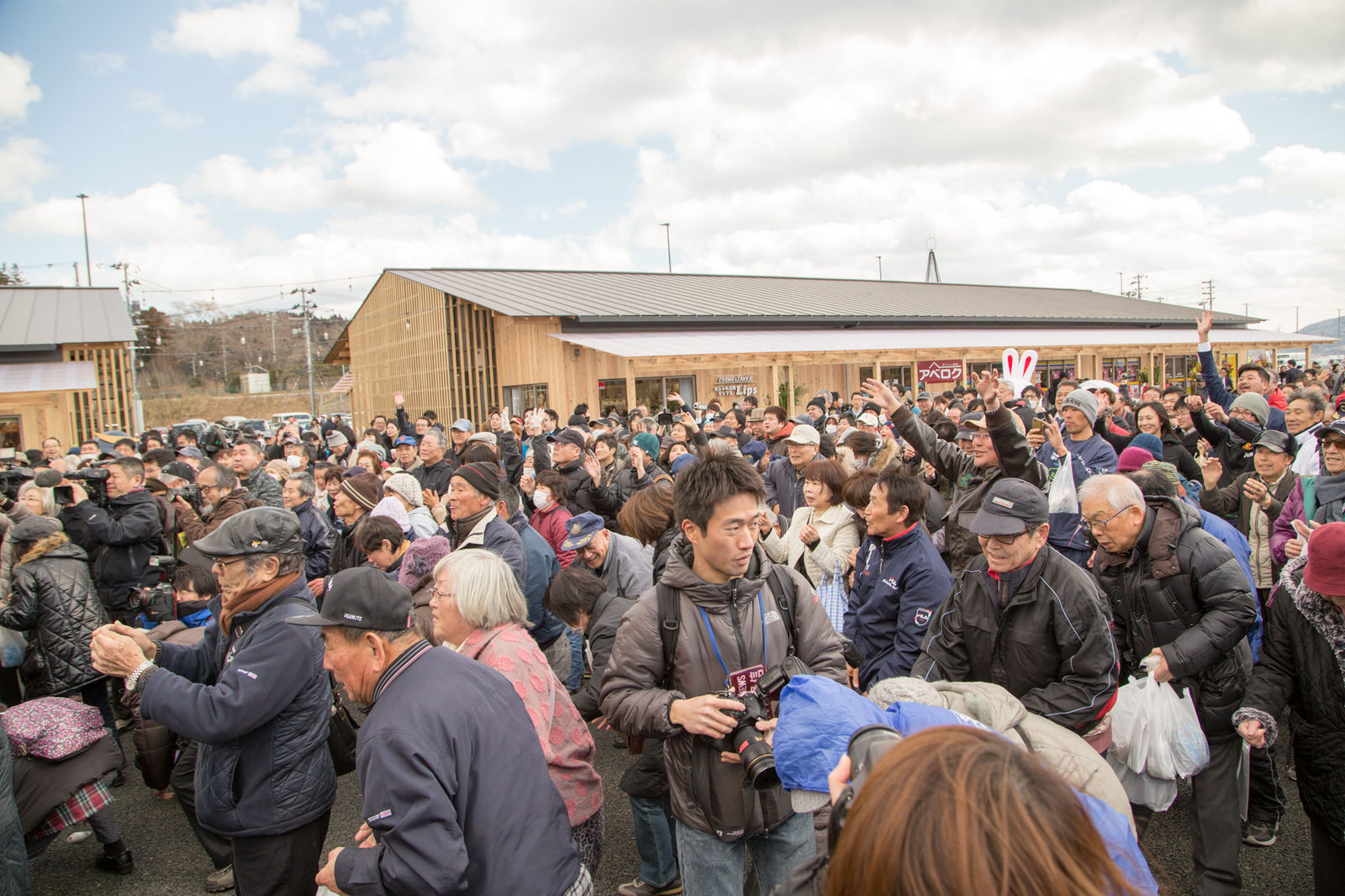 オープンした商店街の屋外に多くの人々が集まっており、投げられた餅をつかもうと手を挙げているにぎわいの様子の写真
