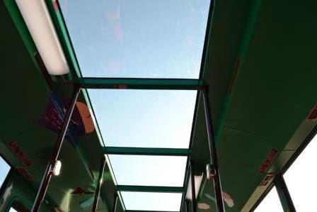 緑色で縁取られたガラス天井から自然光が差し込み、両側に蛍光灯が設置されたバスの車内を写した写真