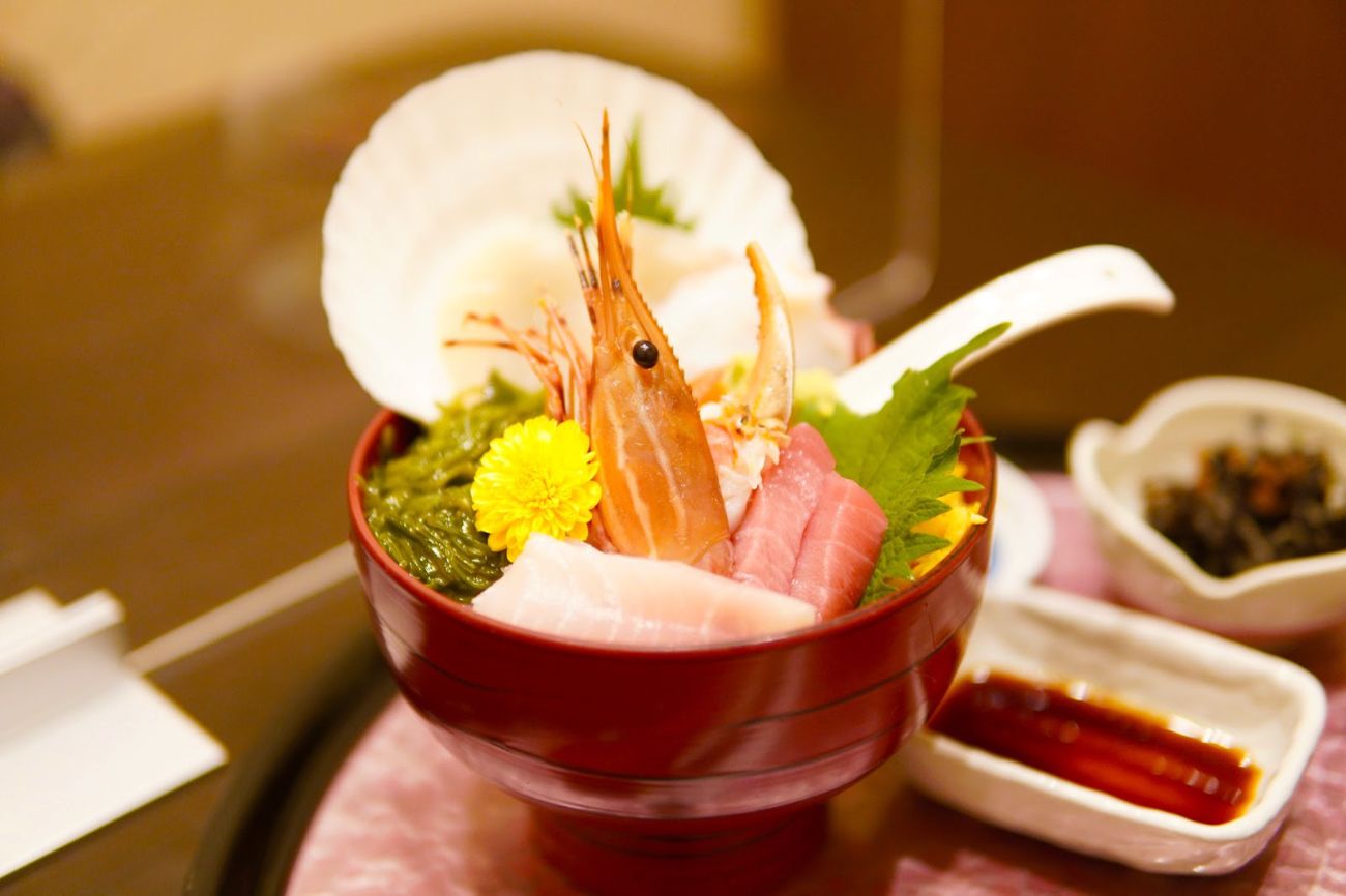 赤い丼に盛られた海老・まぐろ・ホタテなどの刺身と海藻が色鮮やかに盛られている海鮮丼の写真