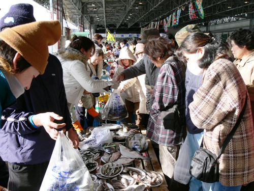 市場で、多くの買い物客が台の上に並べられた皿盛りや平積みされた新鮮な魚介類を品定めしているおすばで祭りの様子の写真