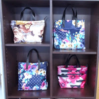 ダークブラウンの棚に、花柄やドット柄などカラフルなトートバッグが4つ並べられている写真