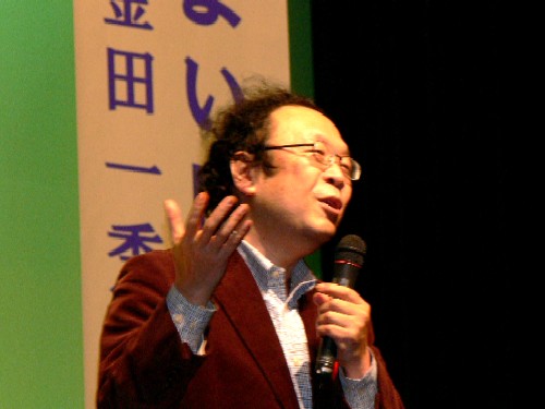 金田一秀穂さんが、マイクを片手に身振り手振りを交えながら話をしている様子の写真