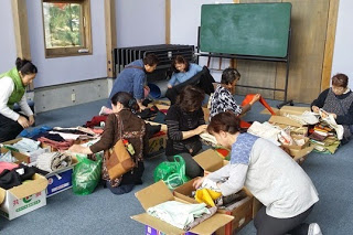 室内で複数の女性が段ボール箱に詰められた着物を手に取り選んでいる様子の写真