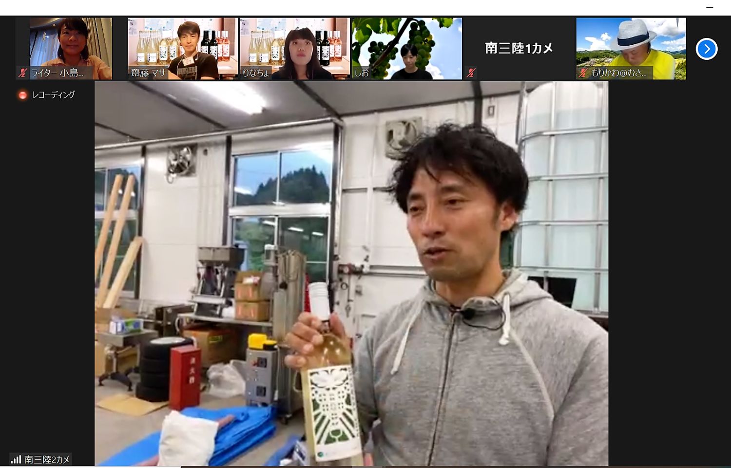 佐々木さん工場のような場所で白ワインのボトルを手に持ち、オンラインツアーに参加している様子の写真