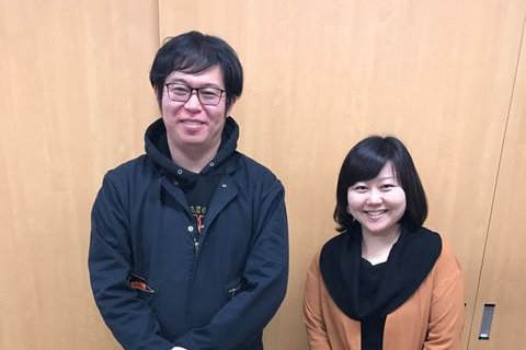 木目調の扉の前に笑顔で並んで立っている女性リポーターと佐藤太一さんの写真