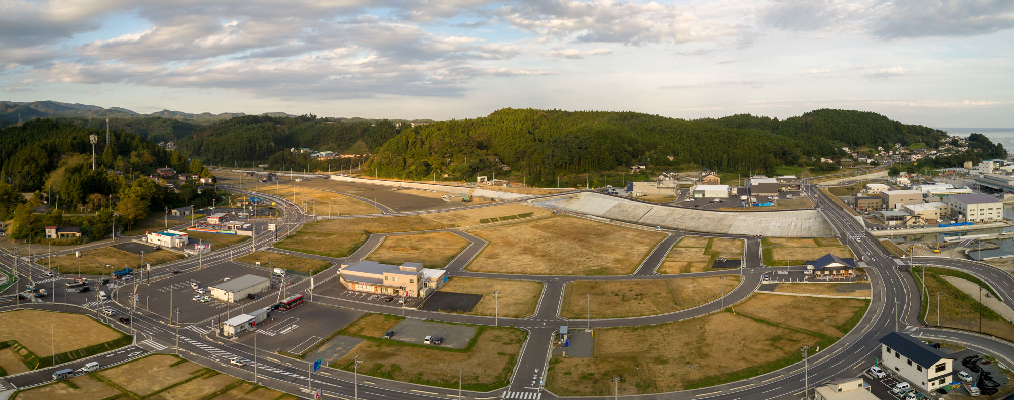 交差点や造成地の更地区画、店舗と道路、海や山が遠景に見える俯瞰写真