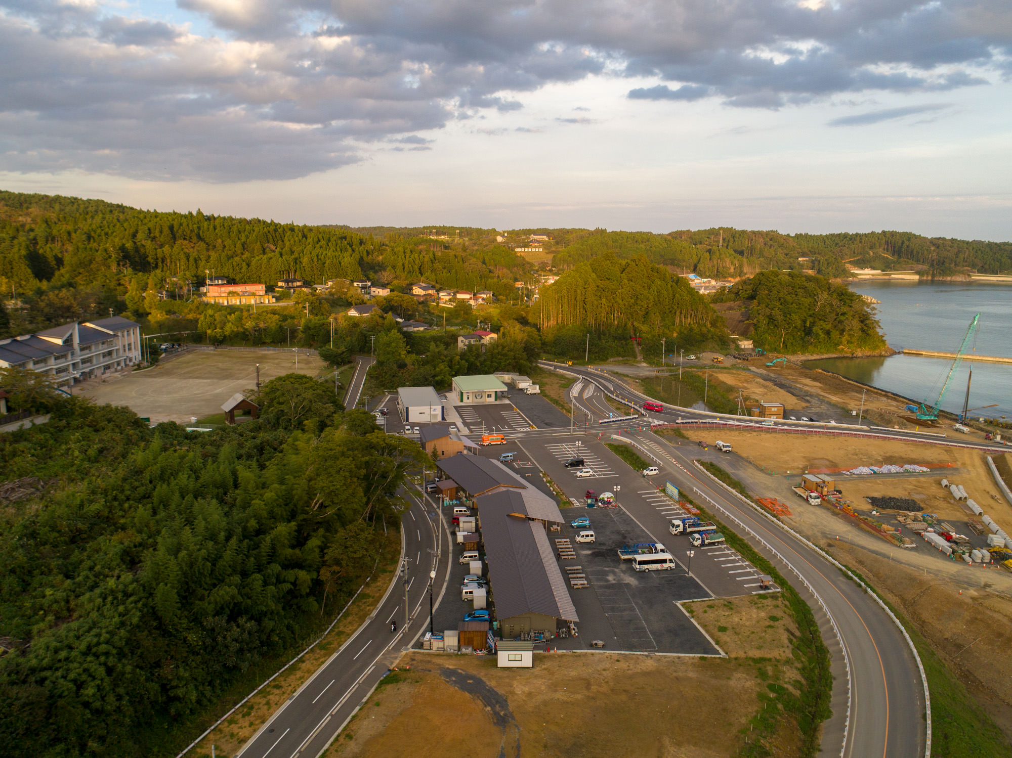 山に囲まれた集落と小学校らしき建物、駐車場と道路が整備された町の中心部を俯瞰でとらえた写真
