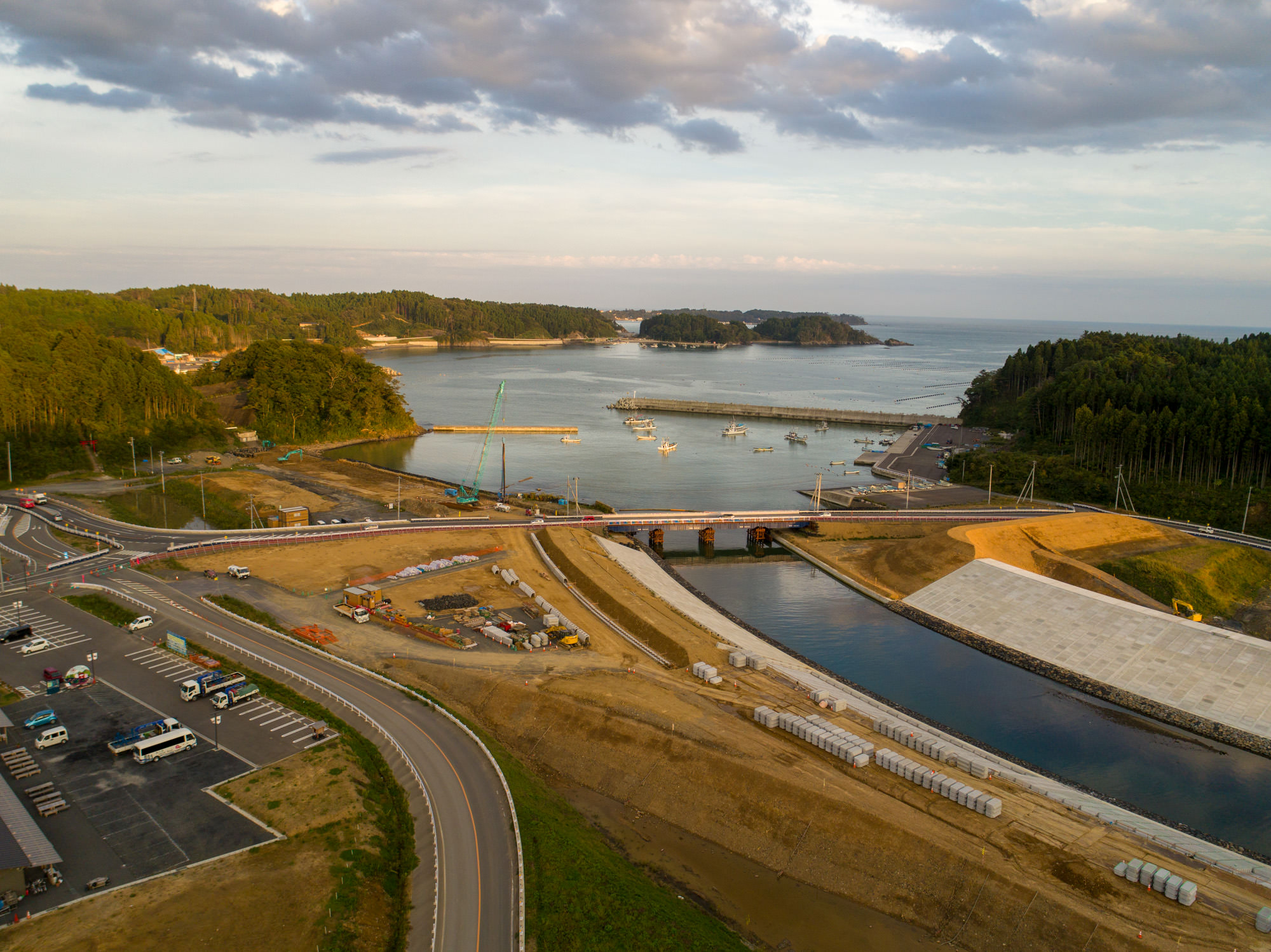 川の河口に架かる橋と港の漁船、背後に広がる海と入り組んだ半島の景観を含んだ町の海側を広く見渡した写真