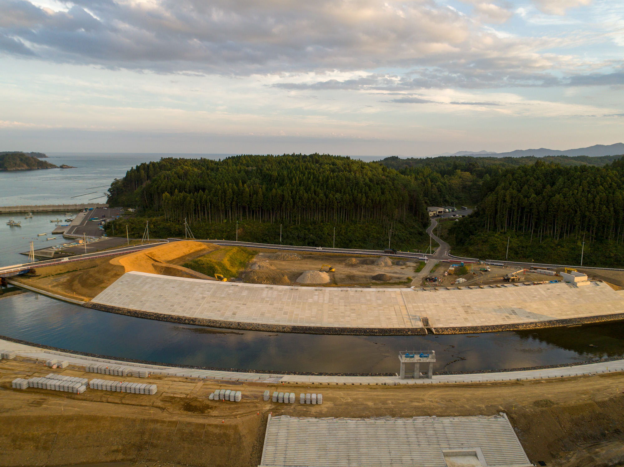 海に注ぐ川の両岸に大型の護岸構造物が整備されており、その奥に港と森が広がっている様子を上空から撮影した写真