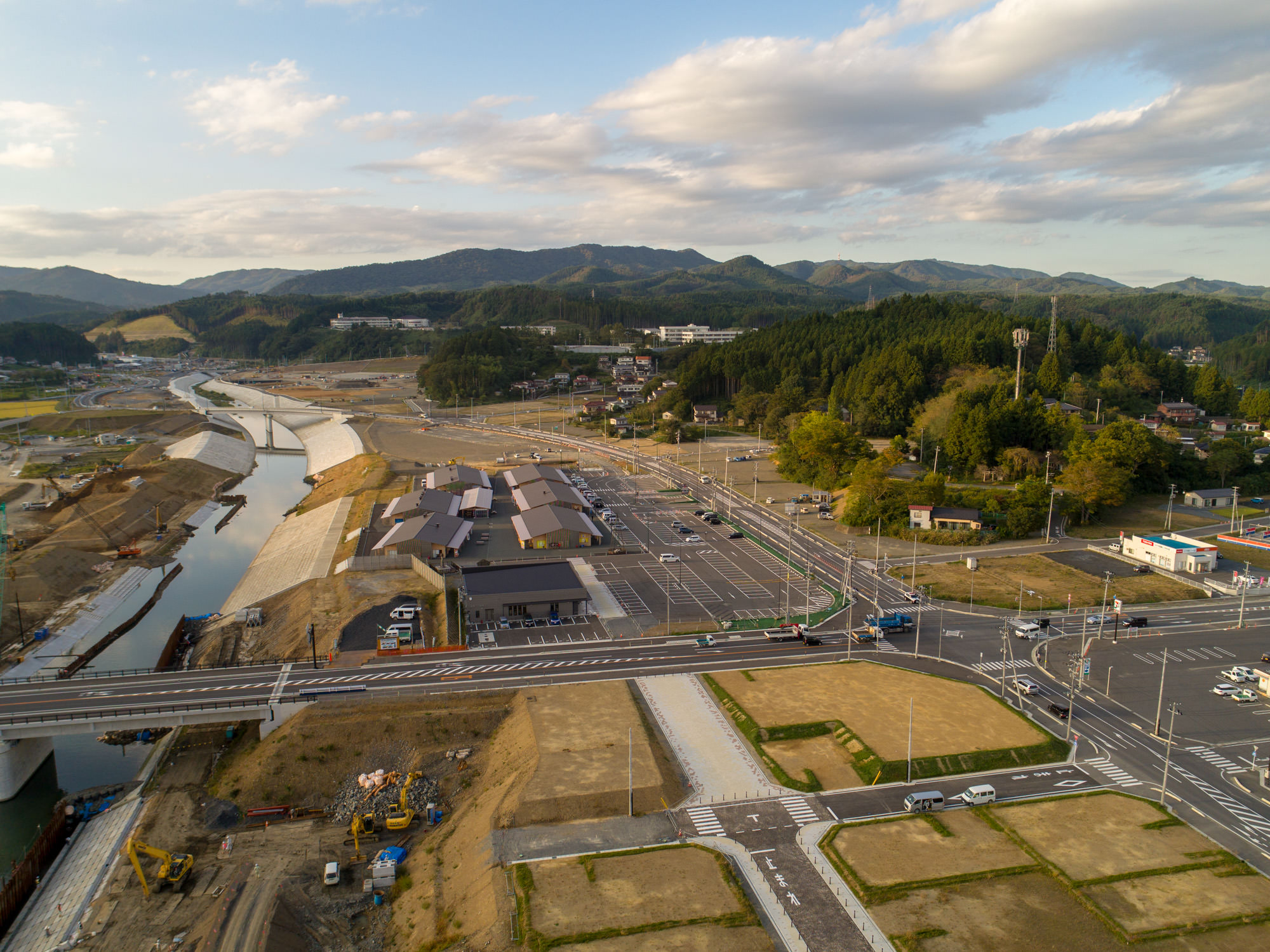 複数の造成区画と交差点、店舗や更地、広い道路と林・山とのコントラストが分かる写真