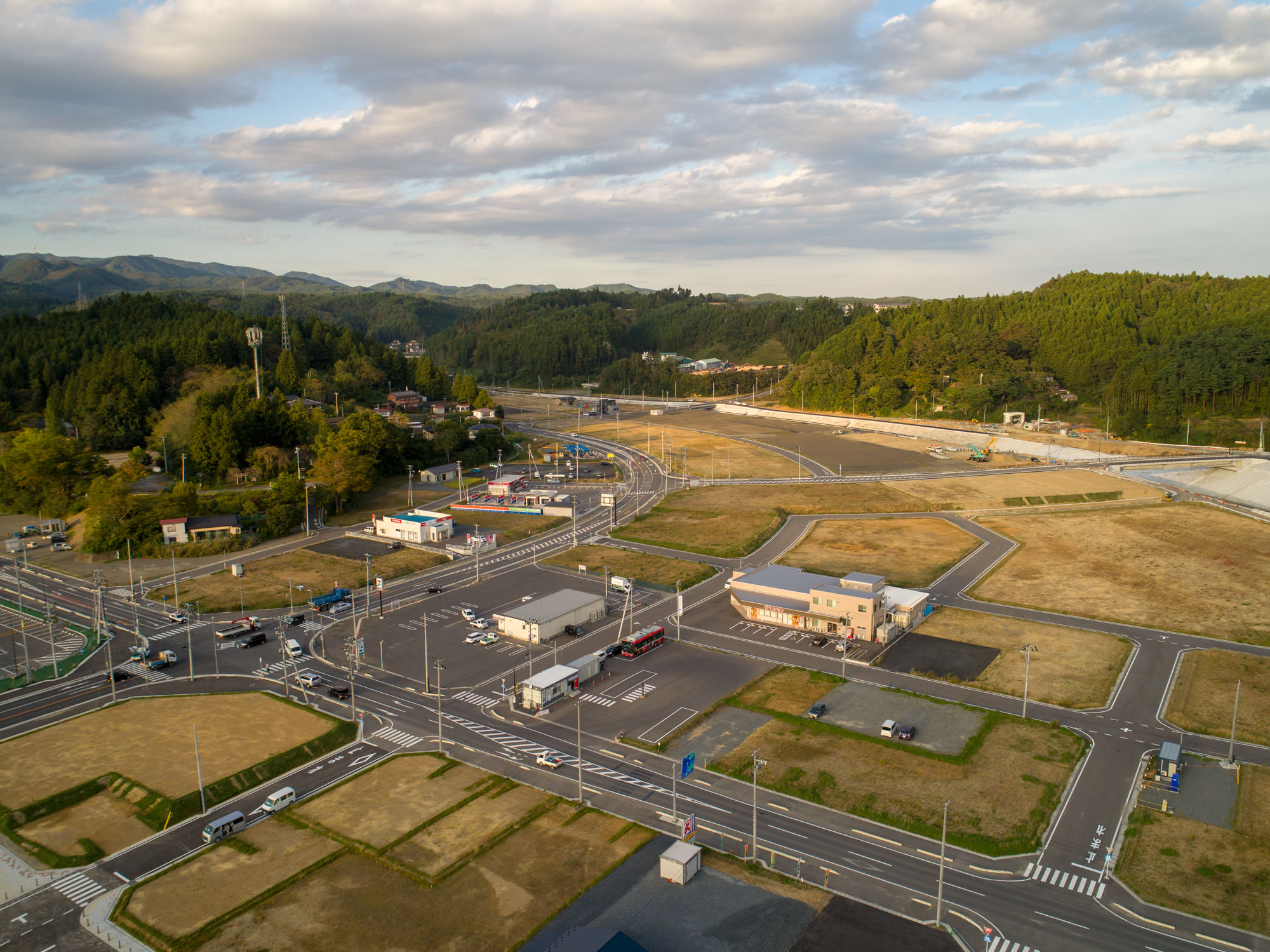 林と山を背に造成整地された更地、道路網で区画された空き地と建物が見える写真