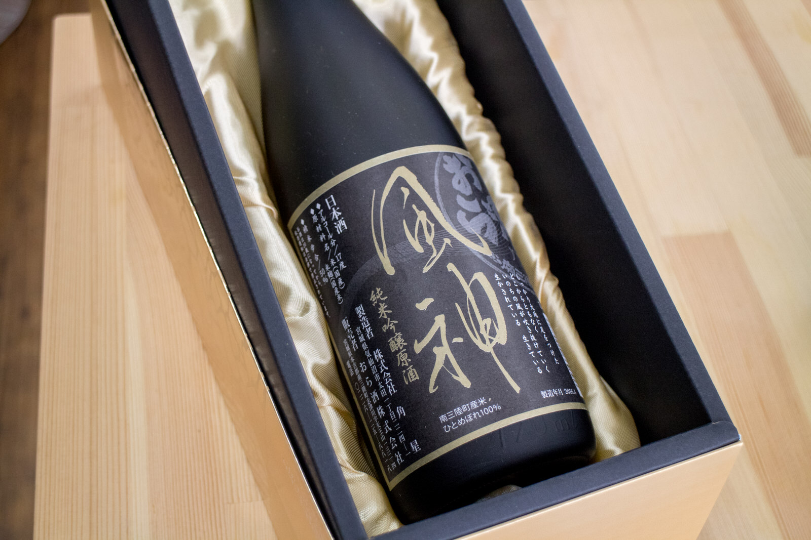 箱の中でベージュのシルクの布の上に「神風」と書かれた黒いラベルがついた、黒い瓶が寝かせて置かれている写真