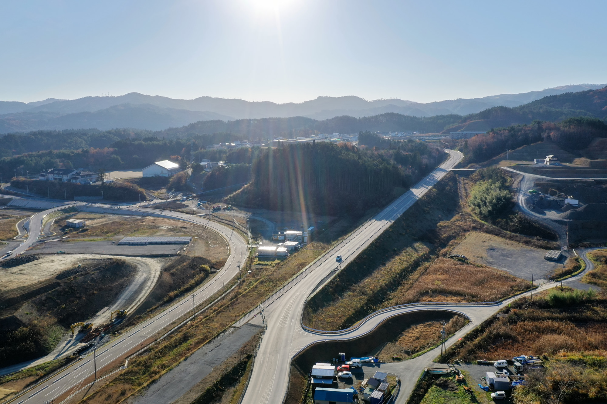 山間部を背景に、複数の道路が立体的に交差しており、その上を車が走行していて、自然の中に交通インフラが整備された様子が見える写真