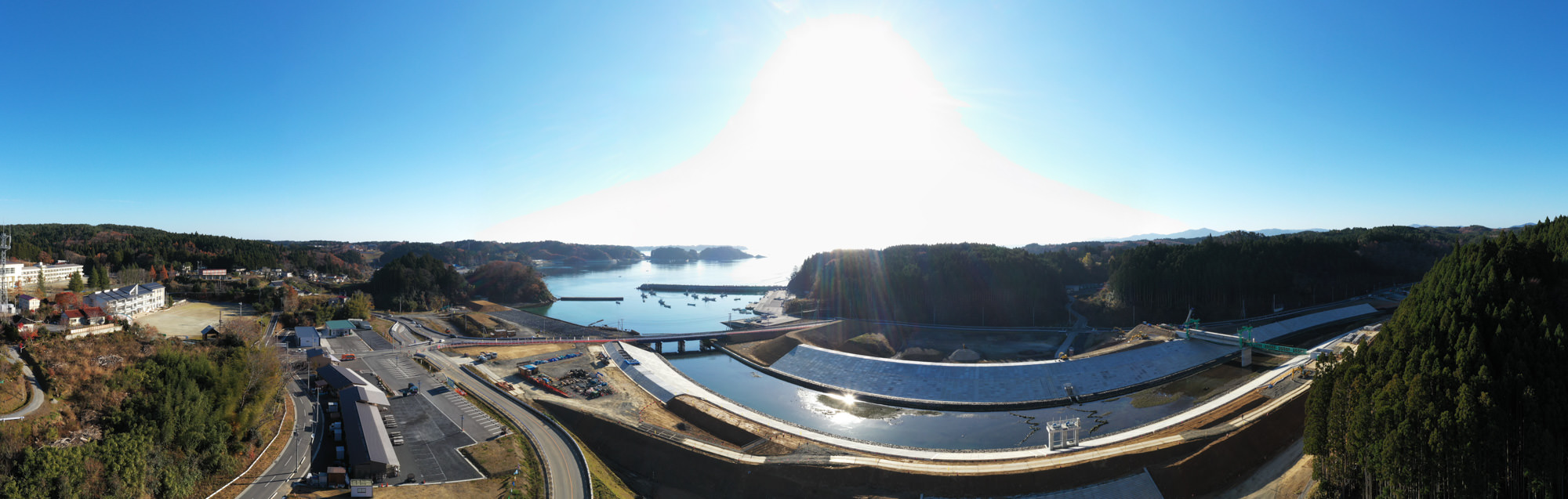 ダムが中央に位置し、その周囲には緑豊かな山々と青空が広がっており、静かな水面が自然の美しさを映し出している風景の写真