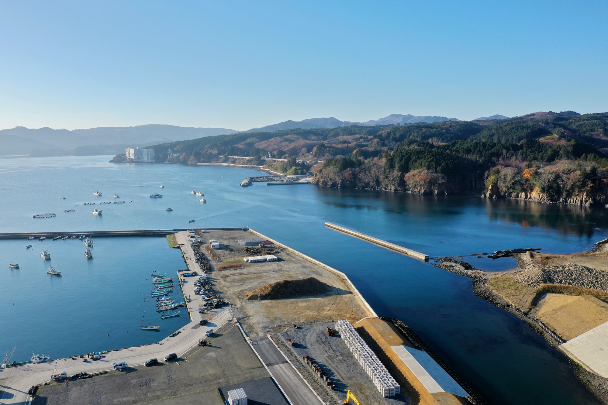 青く澄んだ海に囲まれた港が広がり、その周囲には緑豊かな山々と整然と並ぶ建物が見え、自然と人の営みが調和している様子が見える写真