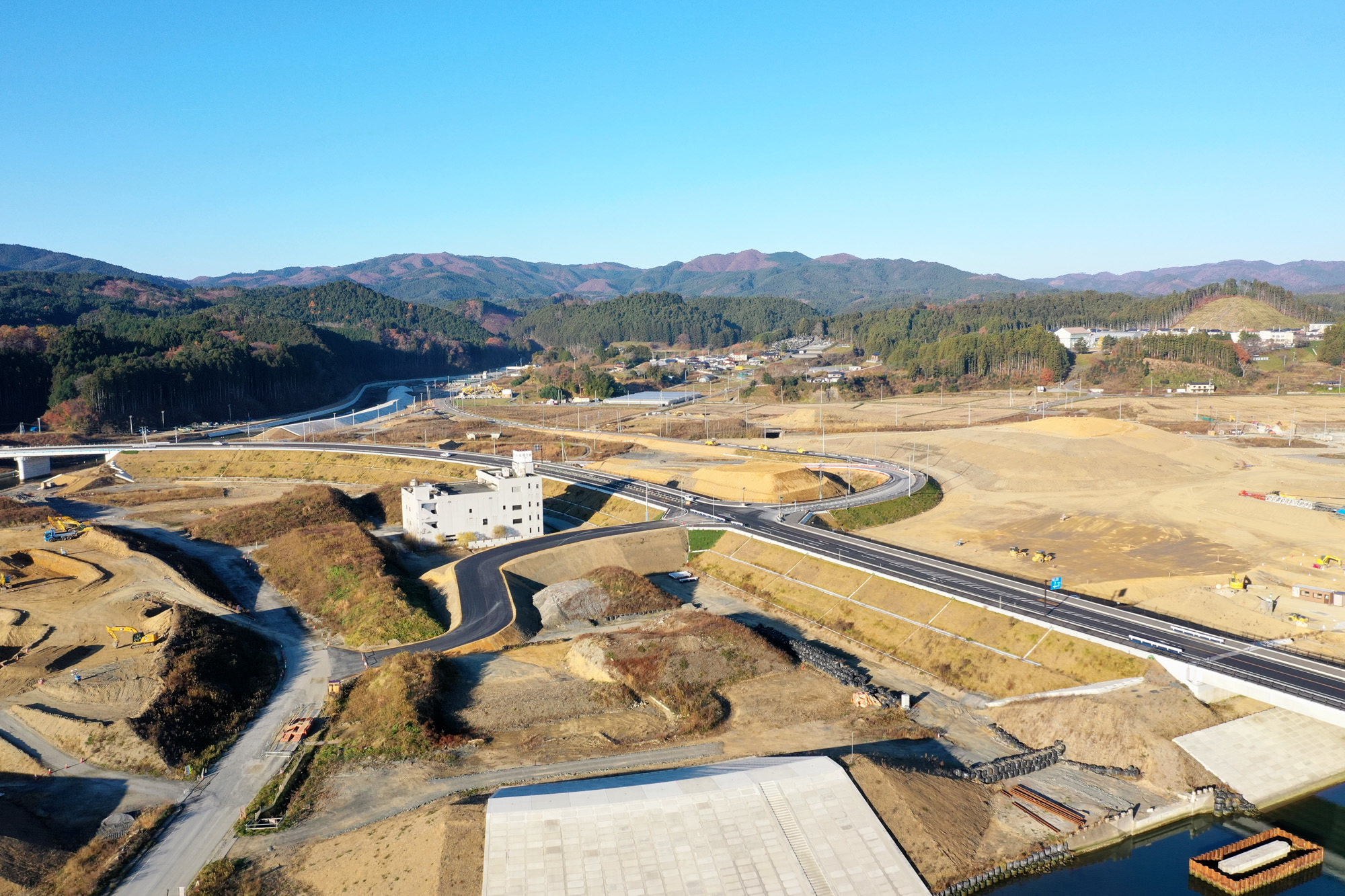 広大な土地に複数の道路が整備されており、周囲には山々が連なり、点在する建物が自然の中に溶け込むように配置されている様子が見える写真