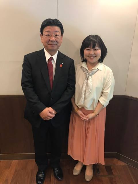 スーツを着た佐藤仁町長と、女性リポーターが並んで笑顔で立っている写真