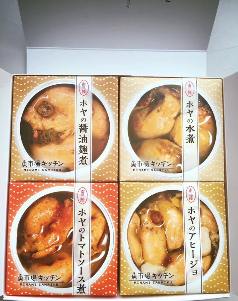南三陸産のホヤの水煮、アヒージョ、醤油麹煮、トマトソース煮の4種の缶詰が箱に詰められたセットの写真