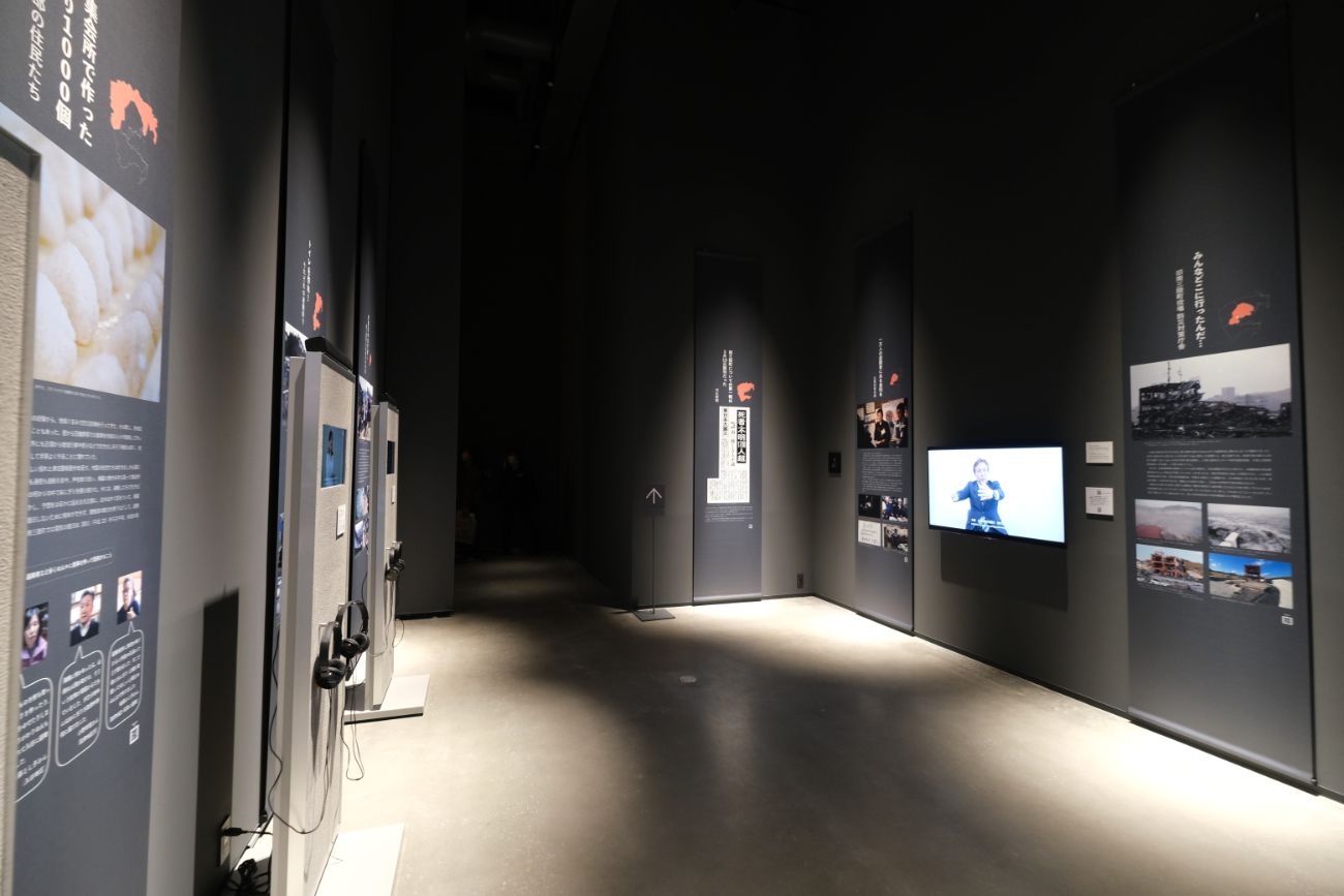 黒いパネルに被災地の写真や地図、証言が展示されており、横にはモニターでインタビュー映像などが流れている展示室内の写真
