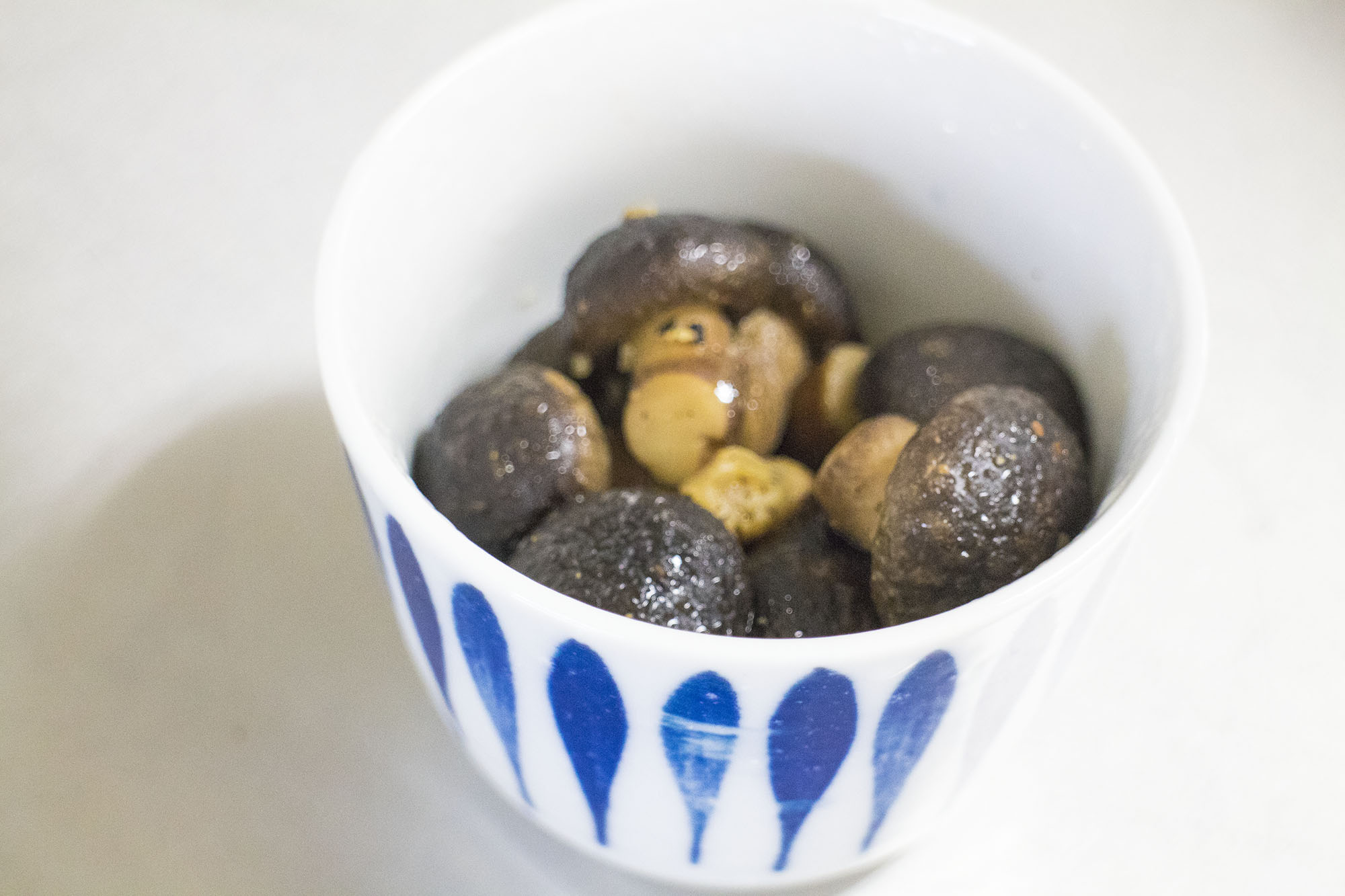 青い模様が描かれた器に、ちいさい椎茸が丸ごと調理された料理が盛り付けられている写真