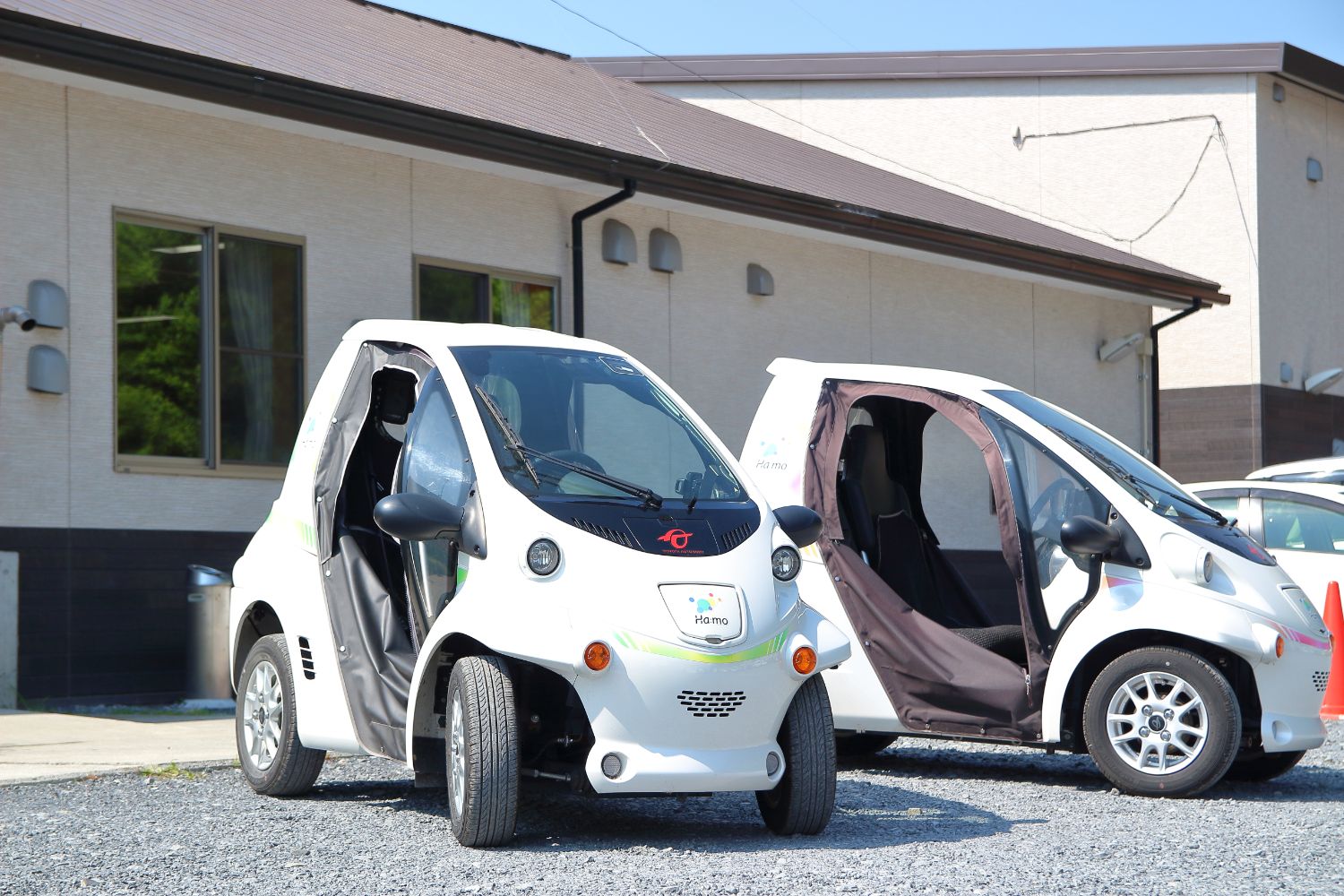 白壁の建物の前に、同じ白い小型電気自動車が2台並んで停まっている写真
