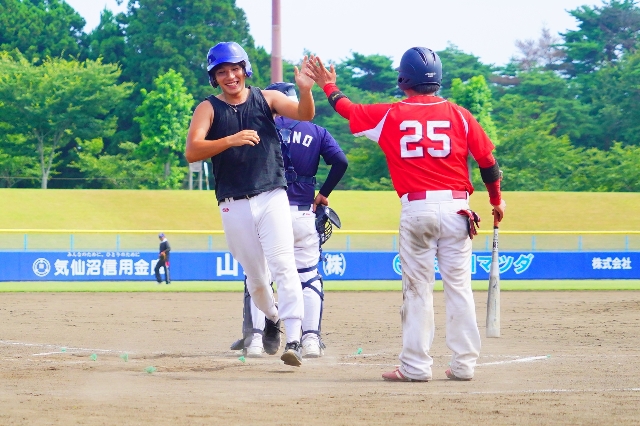 青いヘルメットをかぶった野球選手がホームインし、赤いユニフォームの選手と笑顔でハイタッチしている様子の写真
