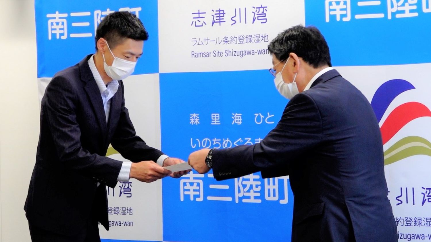 マスクをしたスーツ姿の小林さんが町長から賞状を受け取っている写真