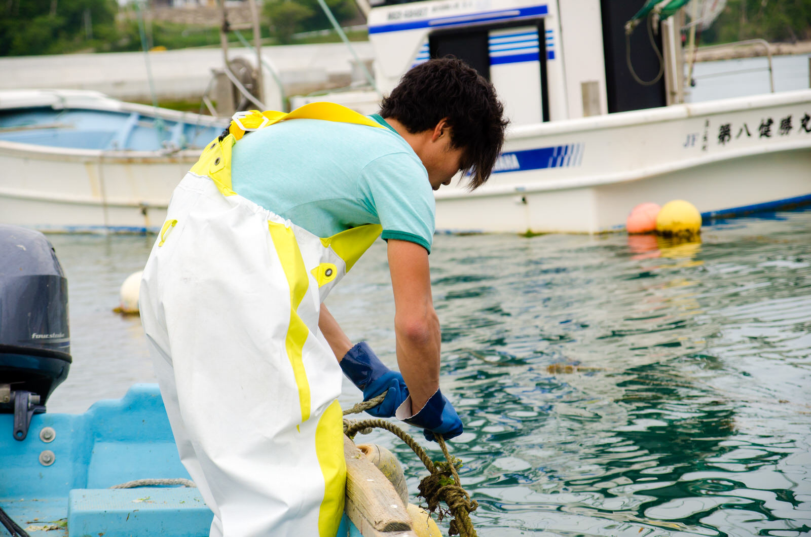 船の縁に立ち、ロープを結ぶ浅野さんの後ろ姿の写真
