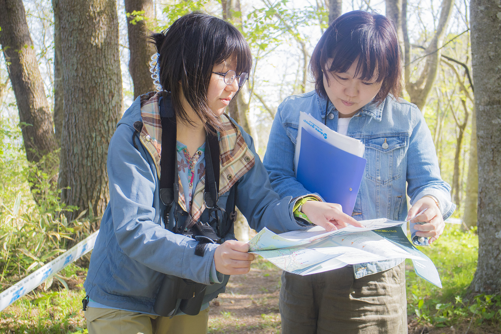 森林の中で、手にした地図を広げ指で示す大渕さんと、地図を見つめる女性リポーターの写真
