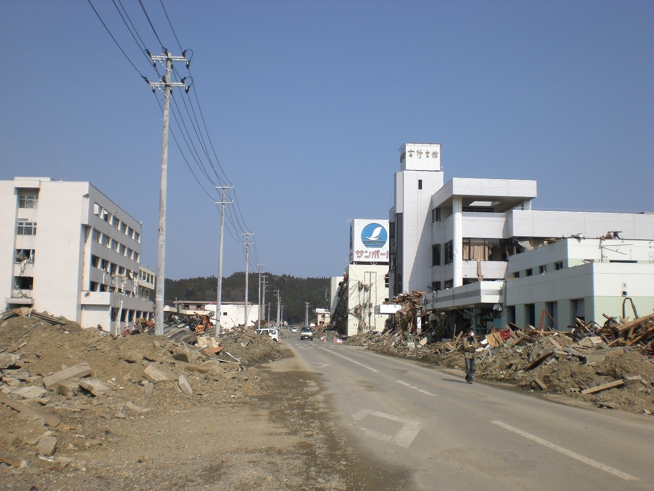 地震によって建物が倒壊し、瓦礫が道路一面に散乱している様子が写っている写真