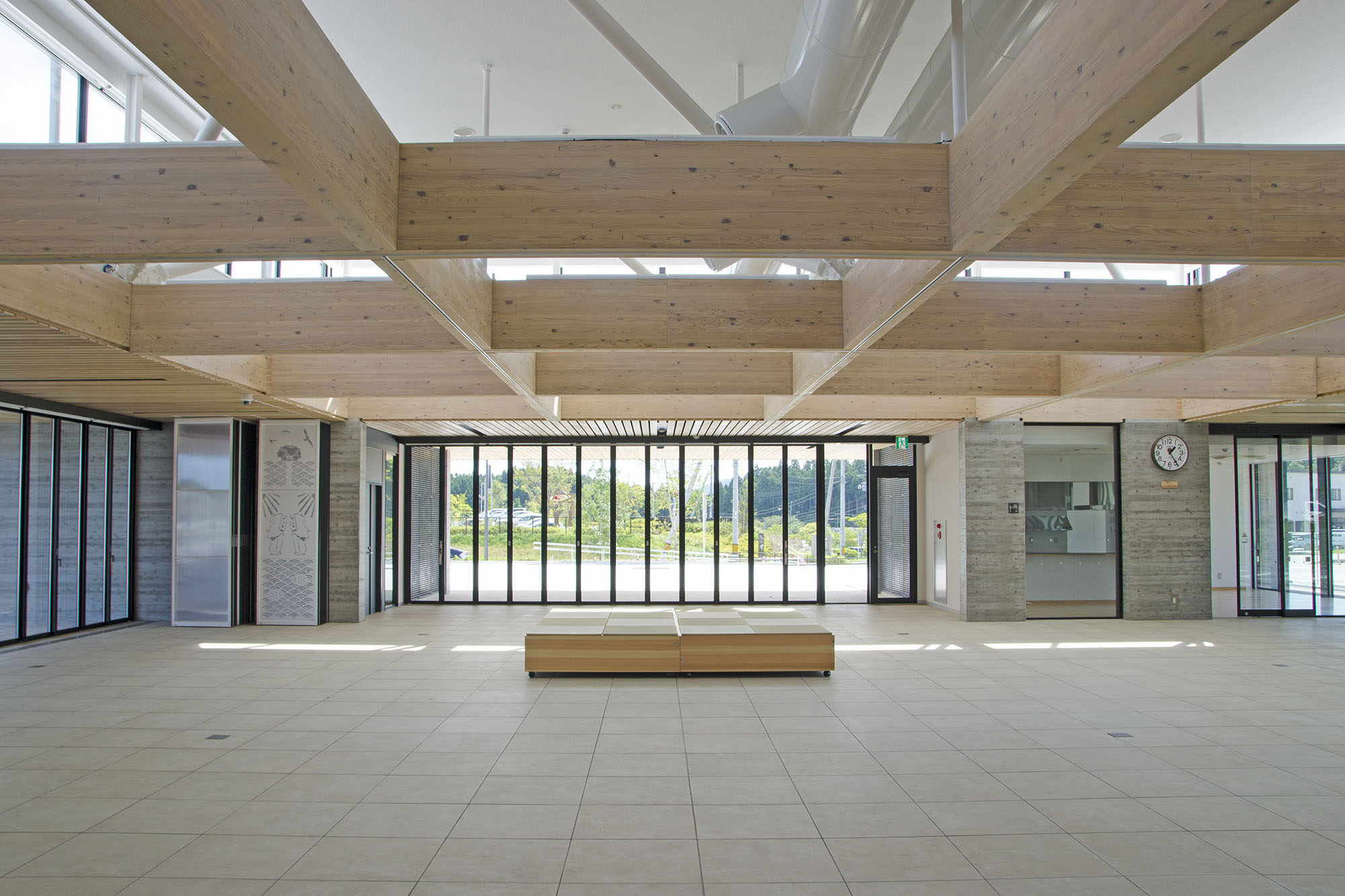 大きな窓から自然光が差し込む、木とコンクリートが調和した開放感のあるロビー空間で、中央にはシンプルなベンチが置かれ、天井には太い木梁が整然と組まれている南三陸町役場新庁舎内の写真