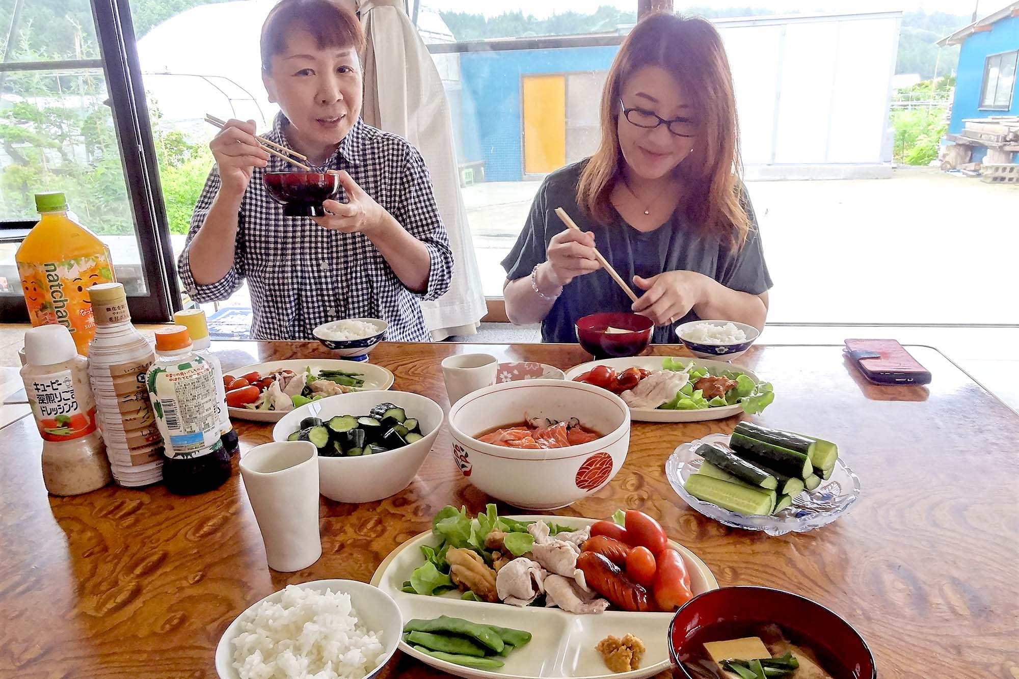 窓際のテーブルで食事を楽しむ2人の女性が、並んだ料理と一緒に楽しそうに食事をしている様子の写真