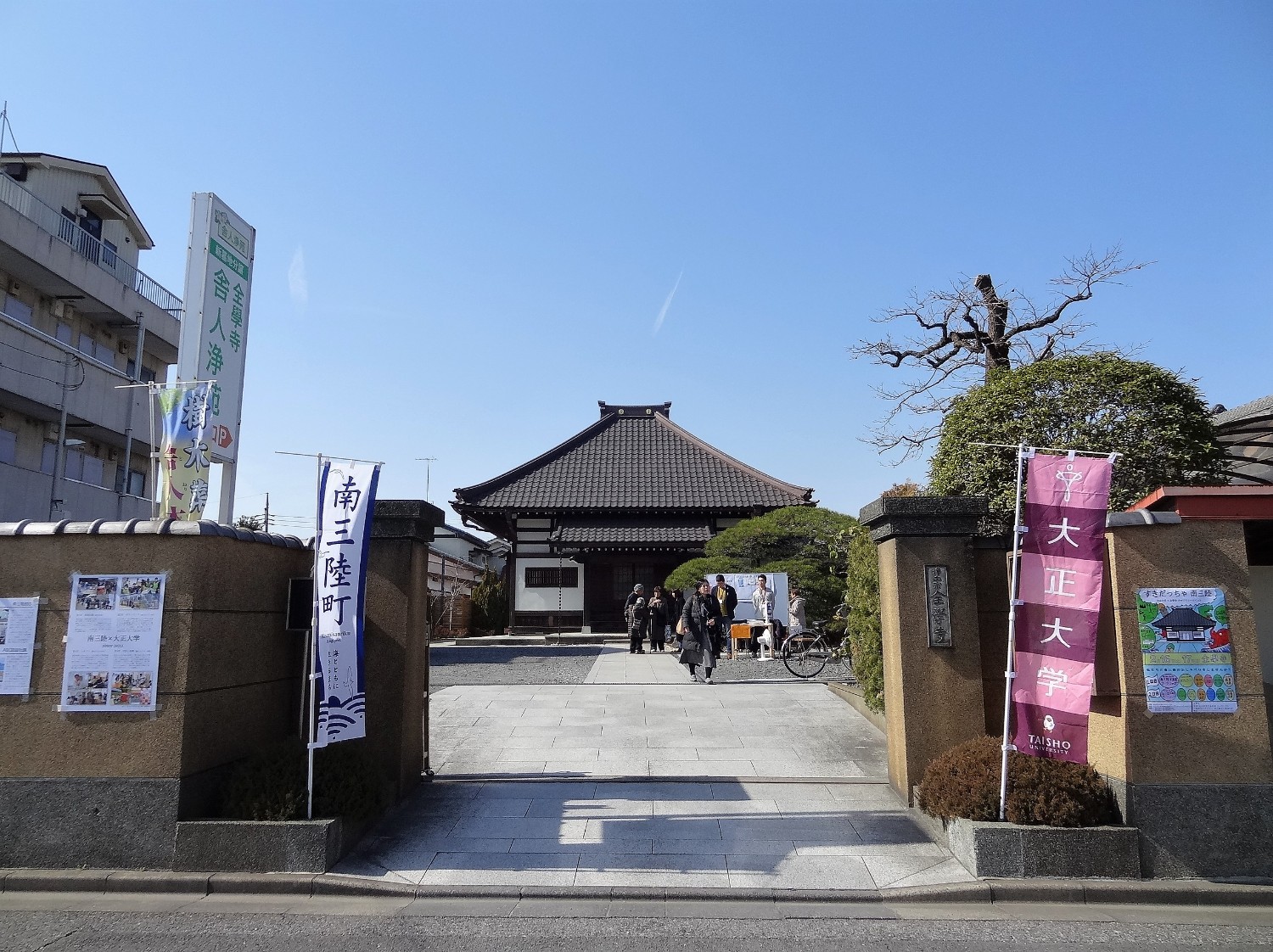 門の両脇に「南三陸町」、「大正大学」と書かれた旗が設置され、門の奥には瓦屋根と木造の構造を持つ伝統的な日本建築が見える写真