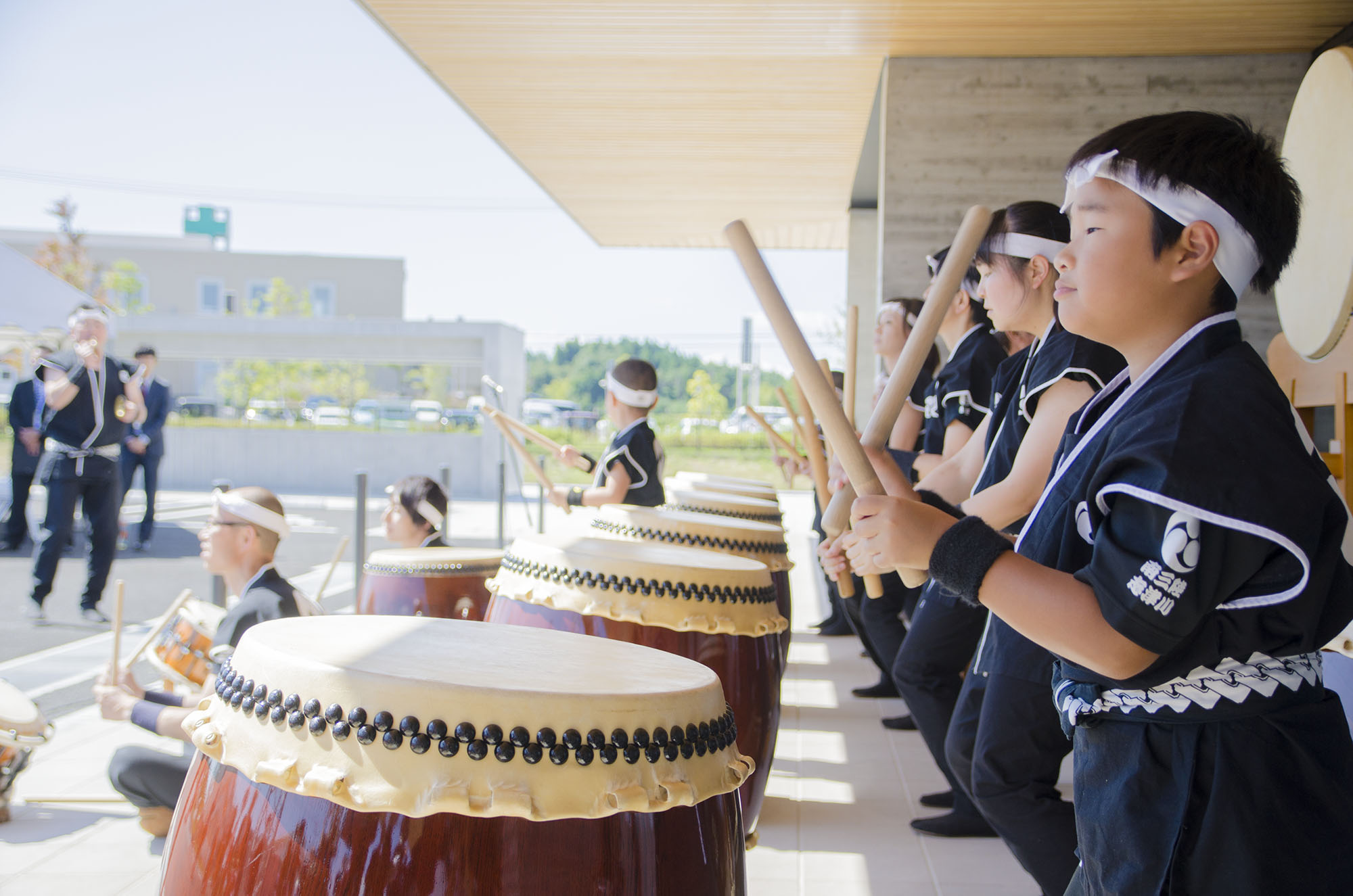 法被姿の子どもや大人たちが、屋外で和太鼓を力強く打ち鳴らしており、晴天の中で南三陸町の新庁舎開庁を祝う演奏を披露している写真