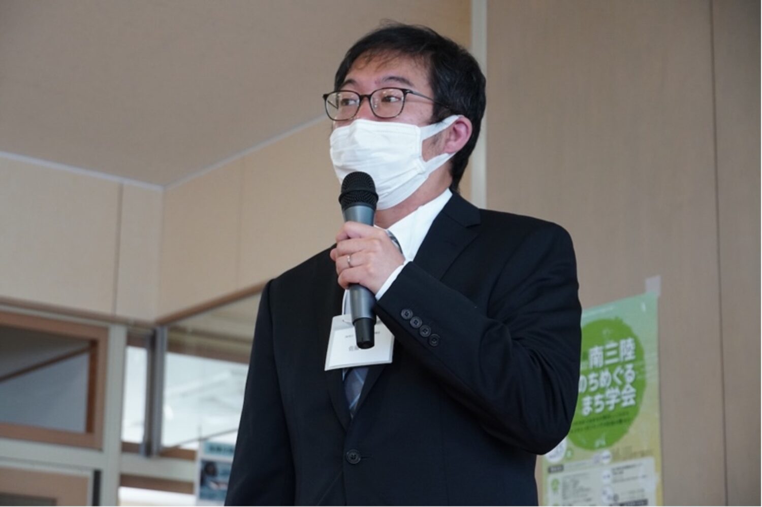 スーツ姿の佐藤太一さんがマイクを持って挨拶をしている写真