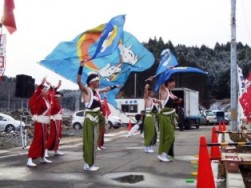 色鮮やかな赤や緑の揃いの衣装を着た人々が大きな旗を振って、踊りを披露している様子の写真