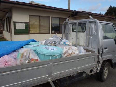 建物の前に停車したトラックの荷台に、複数のゴミ袋やごみ箱が積まれている様子を写した、ごみ分別回収作業中の写真