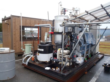 窓のあるコンテナハウスの外に、タンクや配管などがたくさん取り付けられた機械設備が置かれているバイオガス施設の写真